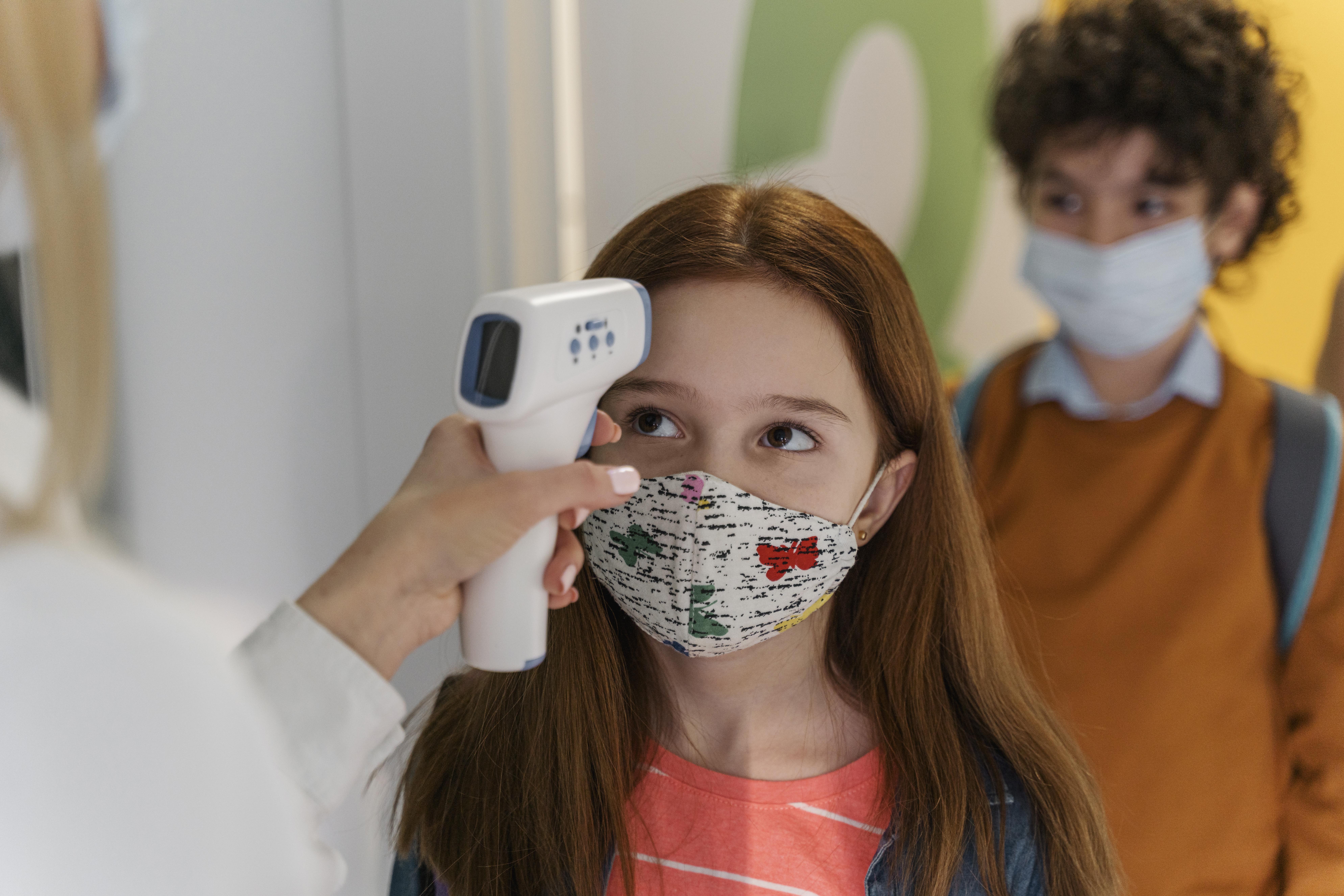 teacher-with-medical-mask-checking-children-s-temperature-in-school